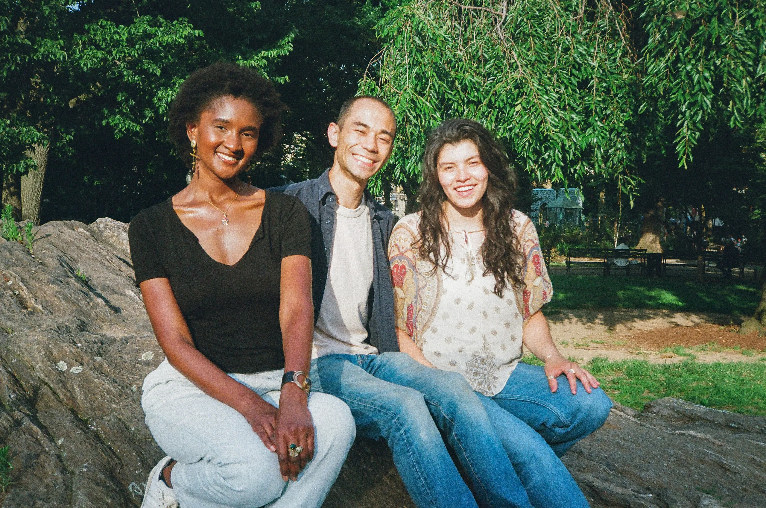 Nandi, David and Fabiola — the Trash Talk NYC team — sitting together on a rock in a park